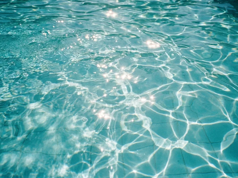 Detalle del agua turquesa cristalina de una piscina con reflejos del sol